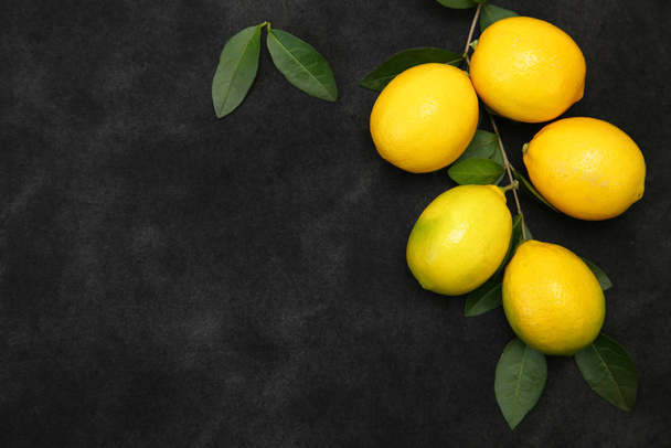 Sappige citroenen op een tak met groene bladeren op een zwarte achtergrond. Biologische vruchten voor een gezond dieet. Verticale foto. Met kopieerruimte. Plat gelegd. Bovenaanzicht. - Foto, afbeelding