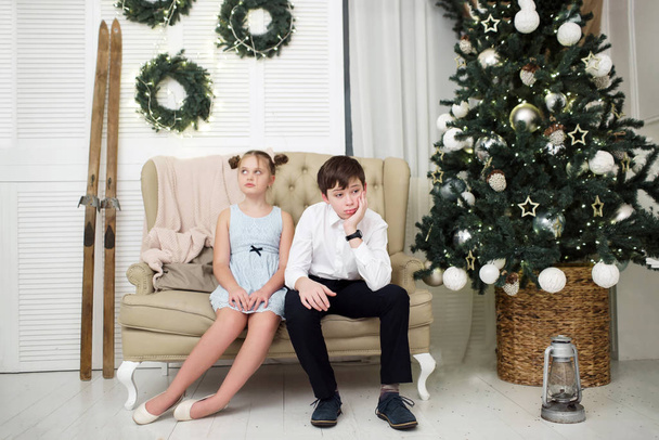 The tortured brother and sister are sitting on the couch by the Christmas tree - Fotoğraf, Görsel