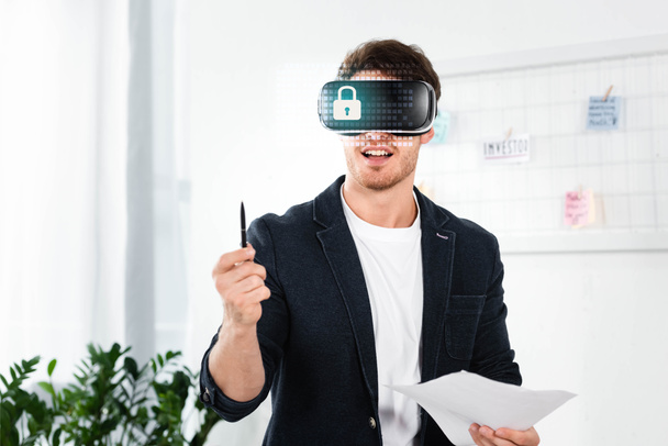 бизнесмен в футболке с гарнитурой виртуальной реальности с иллюстрацией кибербезопасности с ручкой и бумагами
 - Фото, изображение