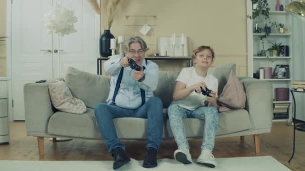 A boy and his grandpa are playing a videogame while sitting on a sofa - Video