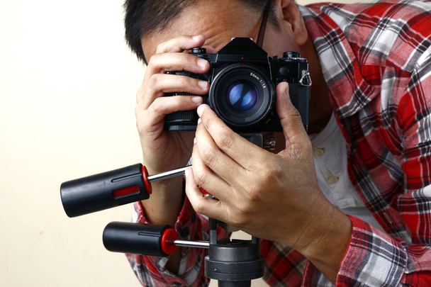 Erwachsener Mann hält eine alte Kleinformat- oder 135mm-Filmkamera auf einem Stativ - Foto, Bild