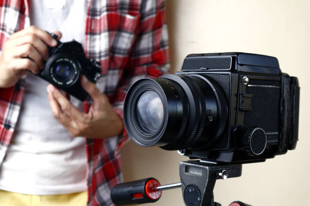 Homme tenant une caméra de film 35mm et se tenant derrière une caméra de film moyen format sur un trépied
 - Photo, image