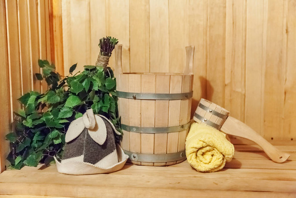 Detail interiéru Finská sauna parní lázeň s tradičním saunovým příslušenstvím povodí březové koště naběračka plstěný klobouk ručník. Tradiční stará ruská lázeňská koncepce lázní. Relax country vesnice lázně koncept - Fotografie, Obrázek