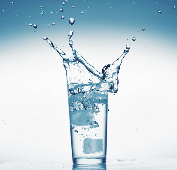 ένα ποτήρι νερό με splash από την πτώση παγάκι, λευκό φόντο, απομονωμένο αντικείμενο - Φωτογραφία, εικόνα