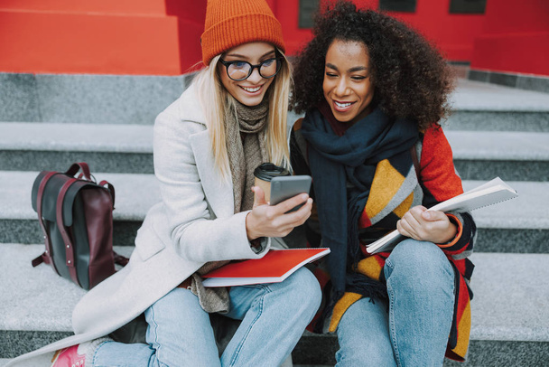 Young Caucasian and Afro American women looking at smartphone - Foto, imagen