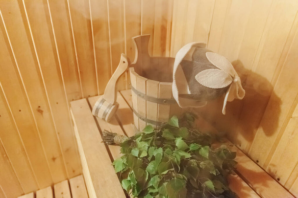 Detalles interiores Sauna finlandesa baño de vapor con accesorios de sauna tradicionales cuenca escoba de abedul escoba sombrero de fieltro. Tradicional antigua casa de baños rusa SPA Concepto. Relajarse pueblo rural concepto de baño
 - Foto, Imagen