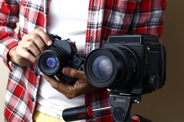 Mies, jolla on 35mm filmikamera ja joka seisoo keskikokoisen filmikameran takana jalustalla
 - Valokuva, kuva