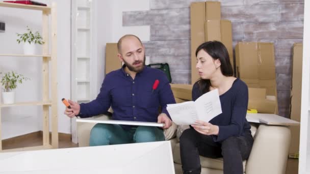 新しいアパートで説明書を使って家具を組み立てるカップル - 映像、動画