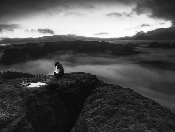 A lány ül a sziklán sötétségben, kezében a remény szimbólumával. - Fotó, kép