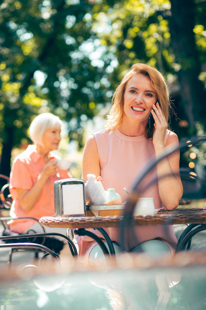 Feliz mujer sonriente en la mesa del café al aire libre disfrutando de una agradable charla telefónica
 - Foto, imagen