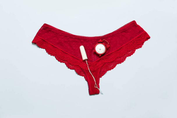 Culotte femme dentelle rouge avec tampon féminin médical contre les jours critiques sur un fond bleu. Menstruations, moyens de protection
 - Photo, image