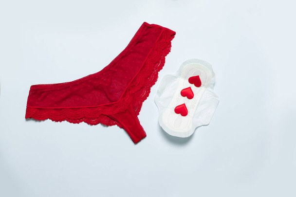Vrouwelijke kant rode slipje met medische vrouwelijke slanke katoen menstruatie pad en liefde vorm tegen kritieke dagen op een blauwe achtergrond. Menstruatie, beschermende uitrusting. - Foto, afbeelding