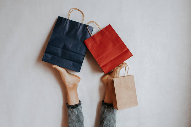 Happy woman holding on feet shopping package. Paper bag. Sale in store. Fashion shop creative advertisement. Customer buy present. Black friday sale. Holiday special offer, discount. Season deal - Fotografie, Obrázek