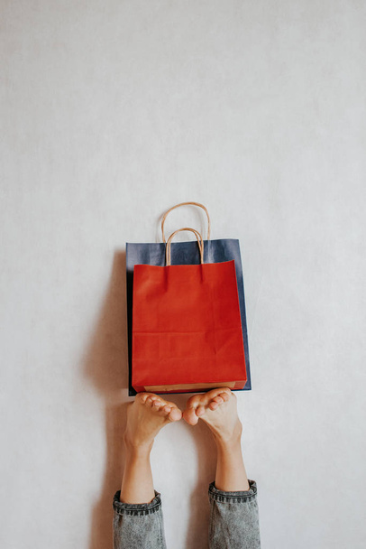Happy woman holding on feet shopping package. Paper bag. Sale in store. Fashion shop creative advertisement. Customer buy present. Black friday sale. Holiday special offer, discount. Season deal - Foto, Imagen