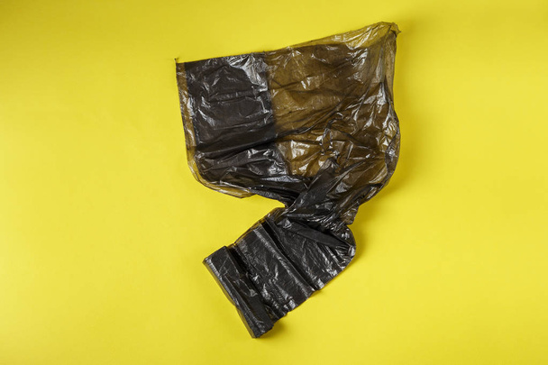 Черный рулон пластиковых мешков для мусора на желтом
 - Фото, изображение