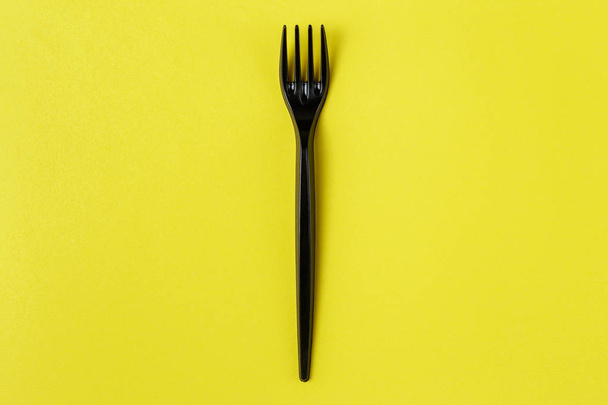 Black plastic fork on yellow background - Fotografie, Obrázek