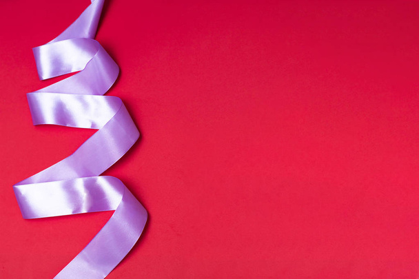 Lilac ribbon on a red background. A wide ribbon folded in a zigzag resembling spruce branches. Picture for christmas, new year with place for text, copy space. - Foto, imagen
