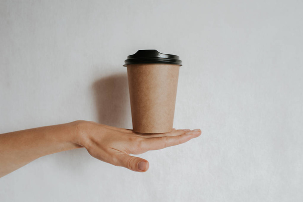 Woman holding in hand paper cup with coffee or tea. Drink coffee time. Disposable paper cup. Beautiful blond hair young girl. Casual style, white shirt and jeans. Take away. Hot beverage. Blank space - Foto, Imagen