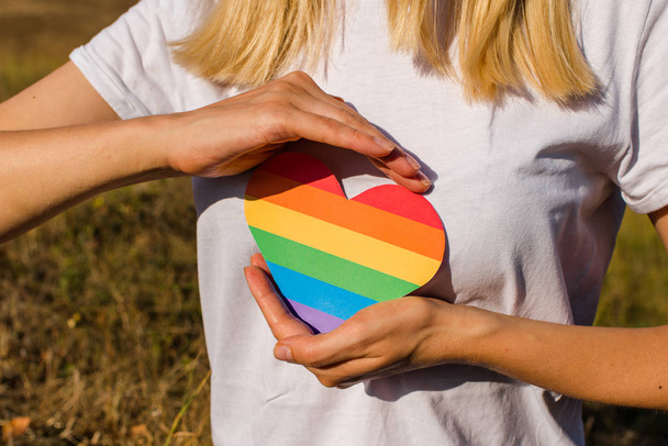 Woman holds in hands a heart in the colors of the rainbow. Young beautiful girl. LGBT history month. Pride Month. Lesbian Gay Bisexual Transgender. LGBT flag. Love, human rights, tolerance. LGBTQ+ - Foto, immagini