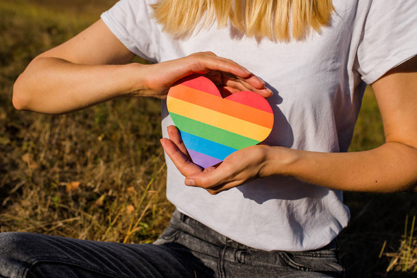 Woman holds in hands a heart in the colors of the rainbow. Young beautiful girl. LGBT history month. Pride Month. Lesbian Gay Bisexual Transgender. LGBT flag. Love, human rights, tolerance. LGBTQ+ - Foto, imagen