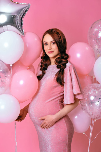 gelukkig zwanger vrouw in roze avond jurk staande op confetti  - Foto, afbeelding