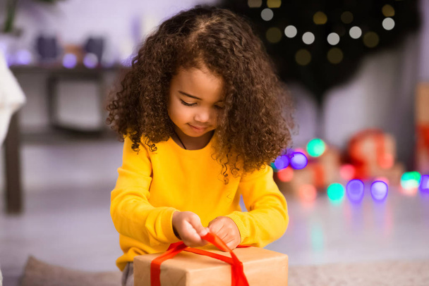 Little african girl opening holiday present on Christmas Eve - Photo, Image