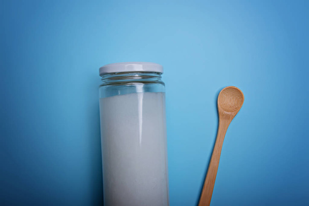 Coconut oil in cream jar and spoon on blue background. - Fotó, kép