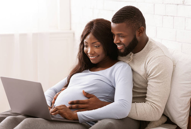 Primer plano de la pareja embarazada negro utilizando el ordenador portátil en casa
 - Foto, Imagen