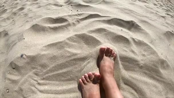Duas pernas de uma menina caucasiana fêmea desfrutando de areia branca em uma praia de areia
 - Filmagem, Vídeo