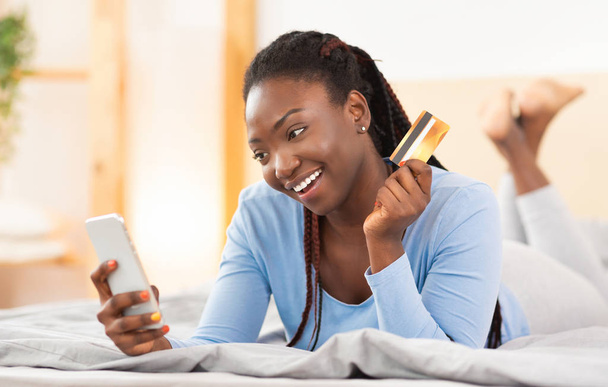 felice nero donna utilizzando telefono acquisto on-line sdraiato a letto
 - Foto, immagini