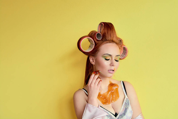 Young redhead woman with shugaring paste on her hands, face, body and chest. Young redhead woman with hair curlers. Advertising concept of shugaring paste. Skin care concept with copyspace. - 写真・画像