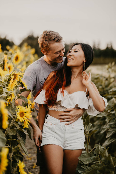 international happy couple hugging in a field of sunflowers at the sunset. Asian girlfriend.  - Photo, image