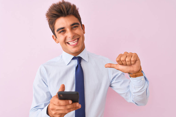 Jonge knappe zakenman met behulp van smartphone staan over geïsoleerde roze achtergrond met verrassing gezicht wijzende vinger naar zichzelf - Foto, afbeelding