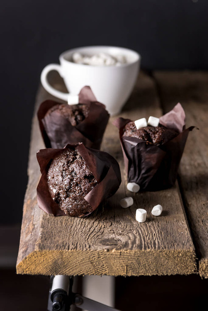 Three Tasty Chocolate Muffins on Wooden Tray White Cup of Cococa with Marshmallow Dark Photo Vertical - Foto, imagen