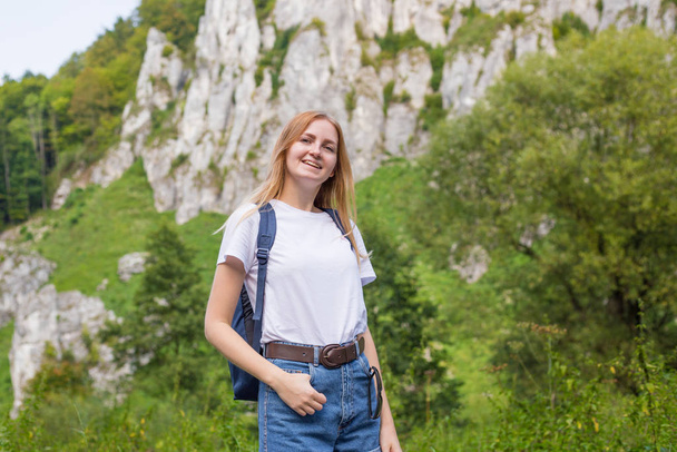 Νεαρή γυναίκα με σακίδιο στέκεται σε ένα φόντο βουνών. Πεζοπορία και τουρισμός έννοια. Αντιγραφικός χώρος. - Φωτογραφία, εικόνα