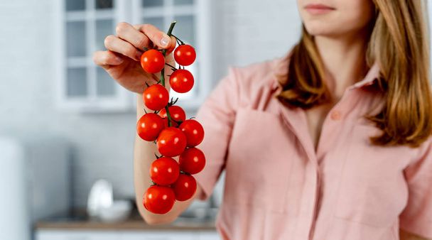 Woman in pink dress is holding branch of ripe cherry tomatoes, closeup - Zdjęcie, obraz