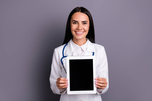 Portrait of experienced doctor woman cardiologist present modern technology black screen tablet she use consult patients wear white coat uniform stethoscope isolated grey color background - Фото, изображение