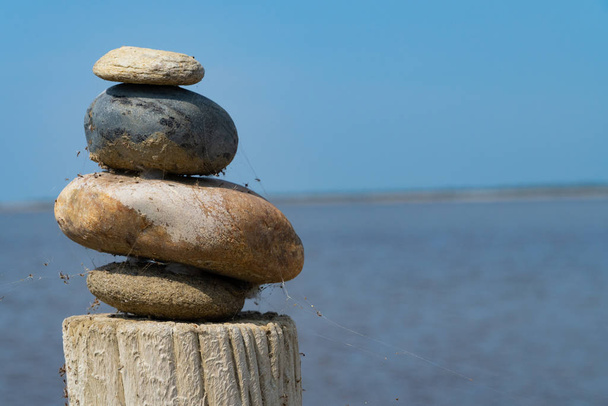 Une pile de pierres colorées sur une colonne en bois devant la mer et le ciel bleu
 - Photo, image