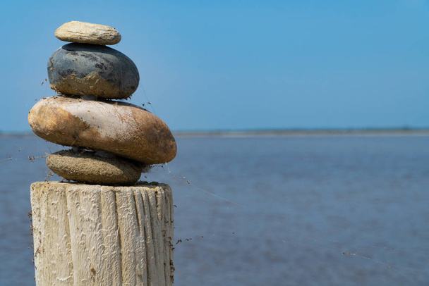 Een stapel kleurrijke stenen op een houten zuil voor de zee en de blauwe lucht - Foto, afbeelding