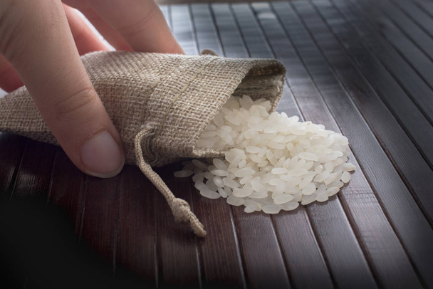 Рука держит соломенный мешок с сырым рисом на деревянном фоне - Фото, изображение