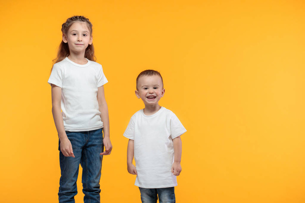 Kid boy and girl wearing white t-shirts with space for your logo or design over yellow texture - Foto, Bild
