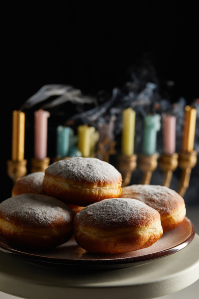 selective focus of delicious doughnuts on stand near candles in menorah isolated on black - Photo, Image