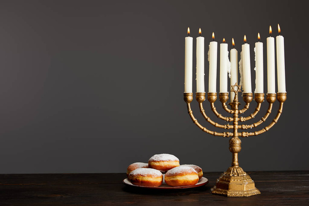 delicious doughnuts near burning candles in menorah on wooden table on Hanukkah isolated on grey - Fotografie, Obrázek
