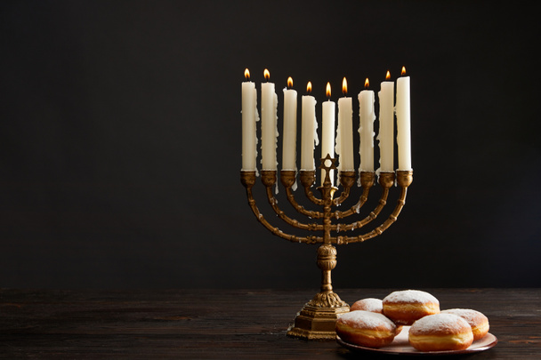 deliciosas rosquillas cerca de velas encendidas en menorah en Hanukkah aislado en negro
 - Foto, imagen
