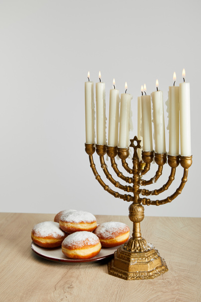 delicious doughnuts near burning candles in menorah on Hanukkah isolated on white - Photo, Image