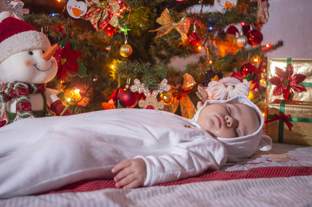 Μωρό που κοιμάται με λευκό φόρεμα και χριστουγεννιάτικο δέντρο - Φωτογραφία, εικόνα