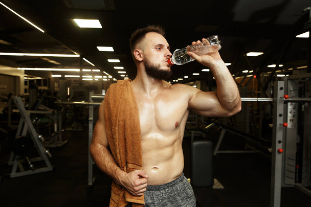 Sporthungriger Mann trinkt Wasser nach dem Regen in der leeren Turnhalle. - Foto, Bild