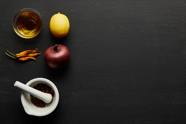 Top view of olive oil, chill peppers with lemon and onion on black wooden background - 写真・画像
