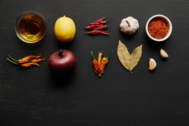 Top kilátás fűszerek, olívaolaj hagymával és citrommal fekete fa háttér - Fotó, kép