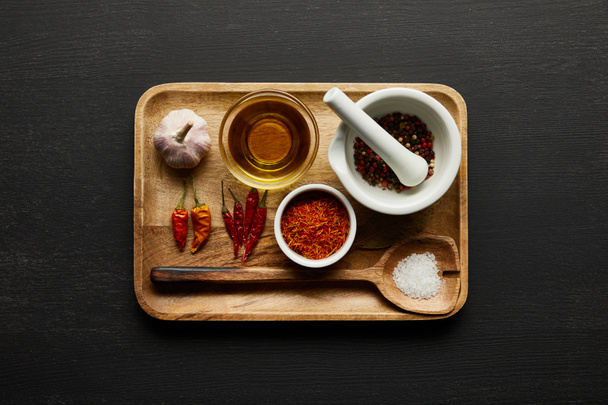 Top view of spices, garlic and olive oil on wooden plate on black wooden background - Фото, изображение
